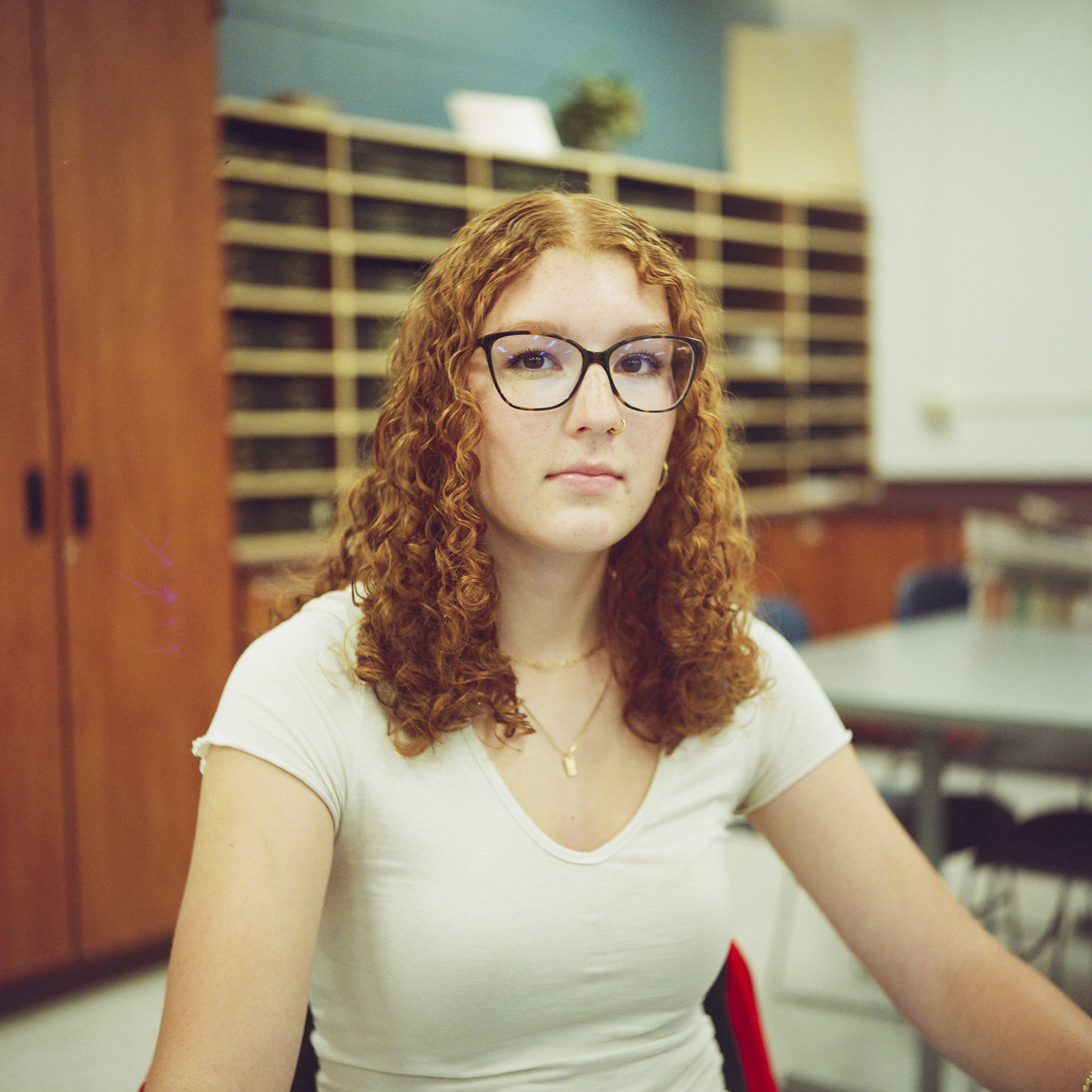 Morgan Stewart poses for a photo while seated in a room with an out-of-focus wood cabinet, shelving and tables with chairs in the background.