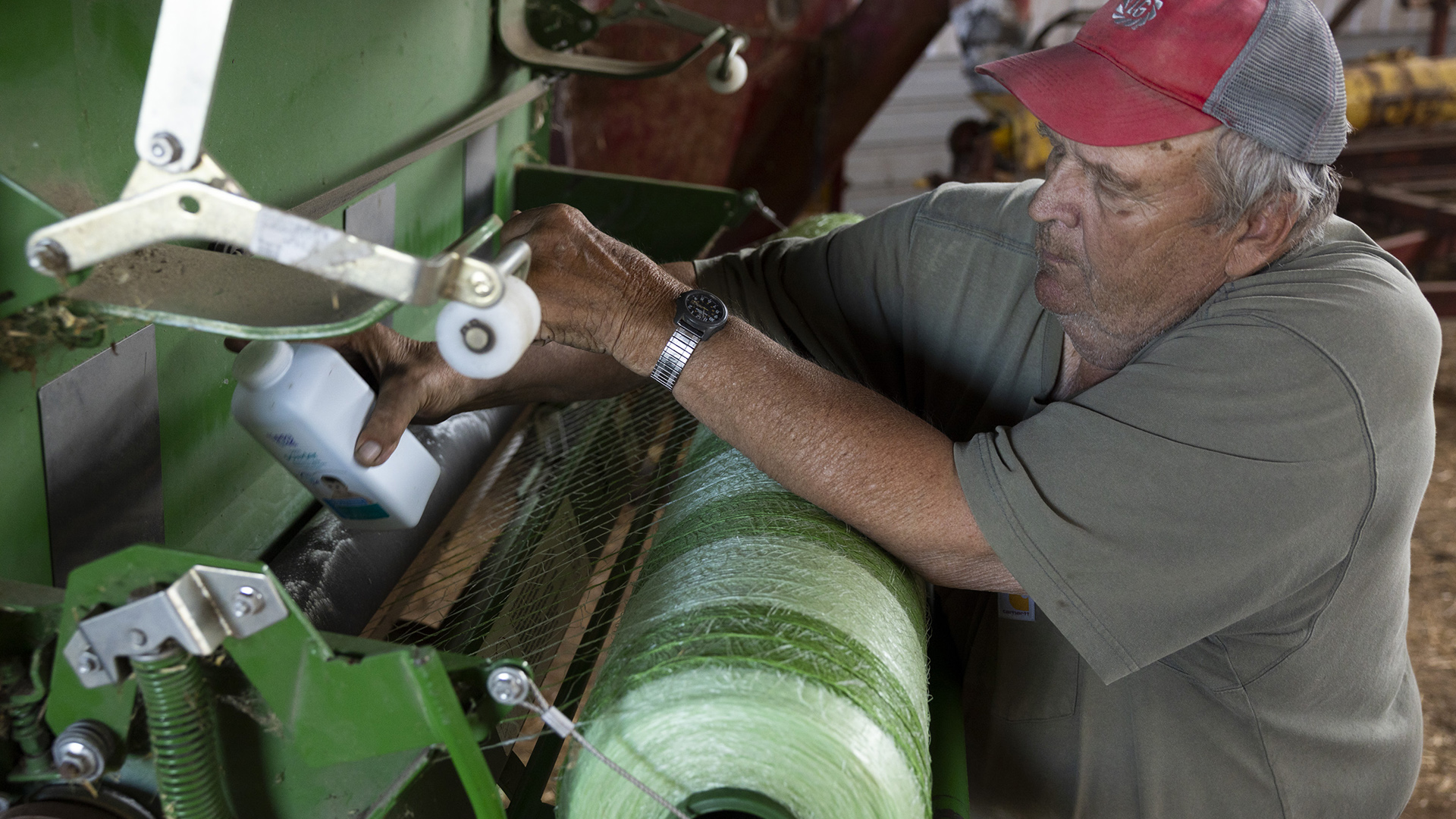 David Hardtke holds a bottle of baby powder in his right hand with his left elbow resting on a roller implement attached to a farm vehicle.