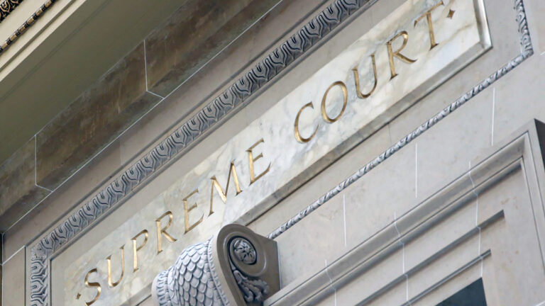 A carved sign reading Supreme Court and a carving of a scroll with scales stands above a doorway under a pediment. A carved sign reading Supreme Court and a carving of a scroll with scales stands above a doorway under a pediment.