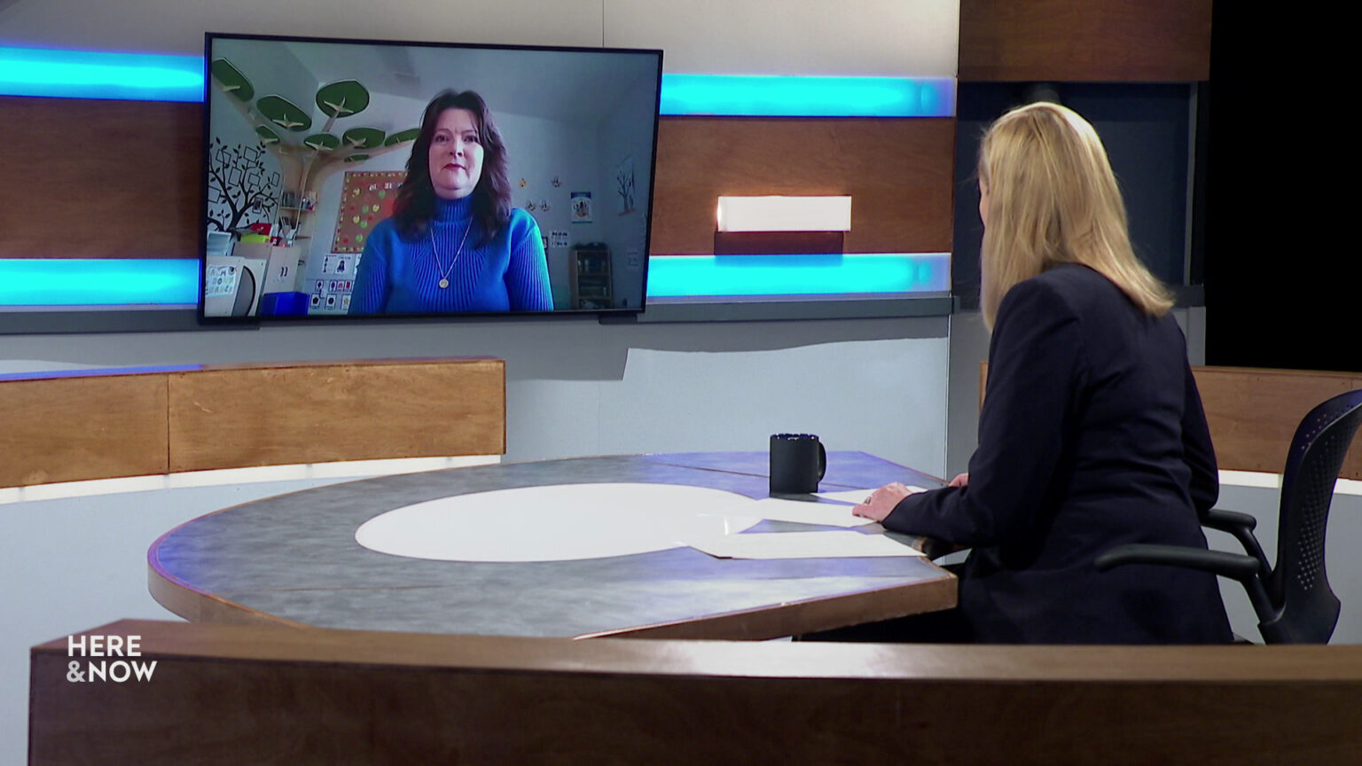 Frederica Freyberg sits at a desk on the Here & Now set and faces a video monitor showing an image of Tawny Hardyman.