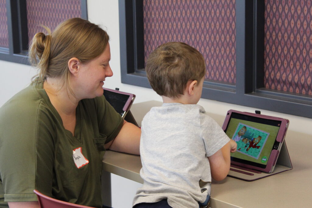A caregiver and young child play on a tablet together