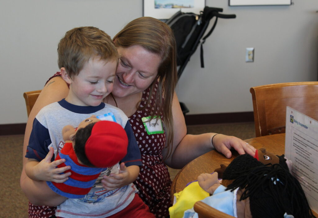 A caregiver and child sit at a table playing with puppets