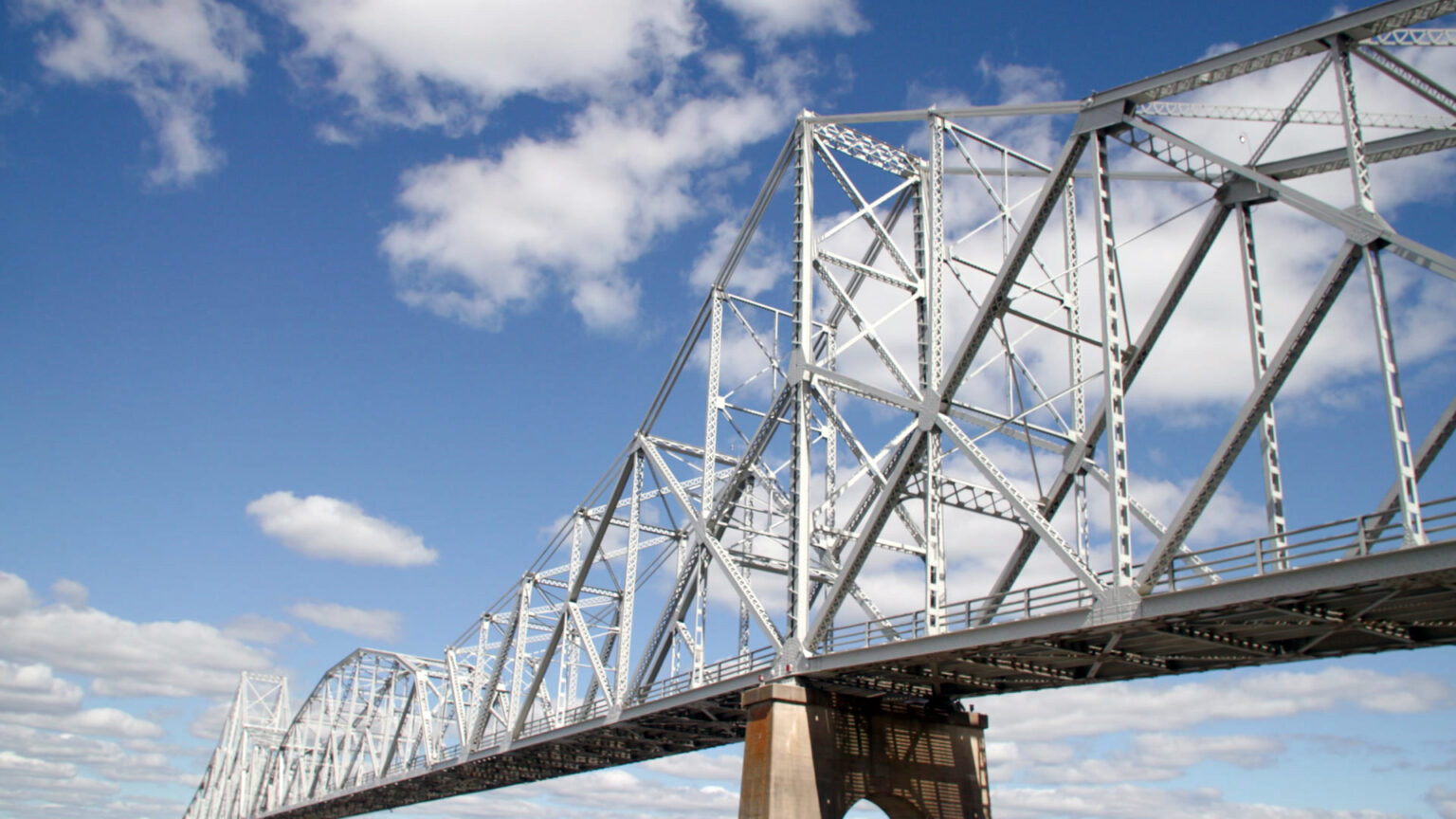Clouds pass over the superstructure of a riveted cantilever metal bridge.