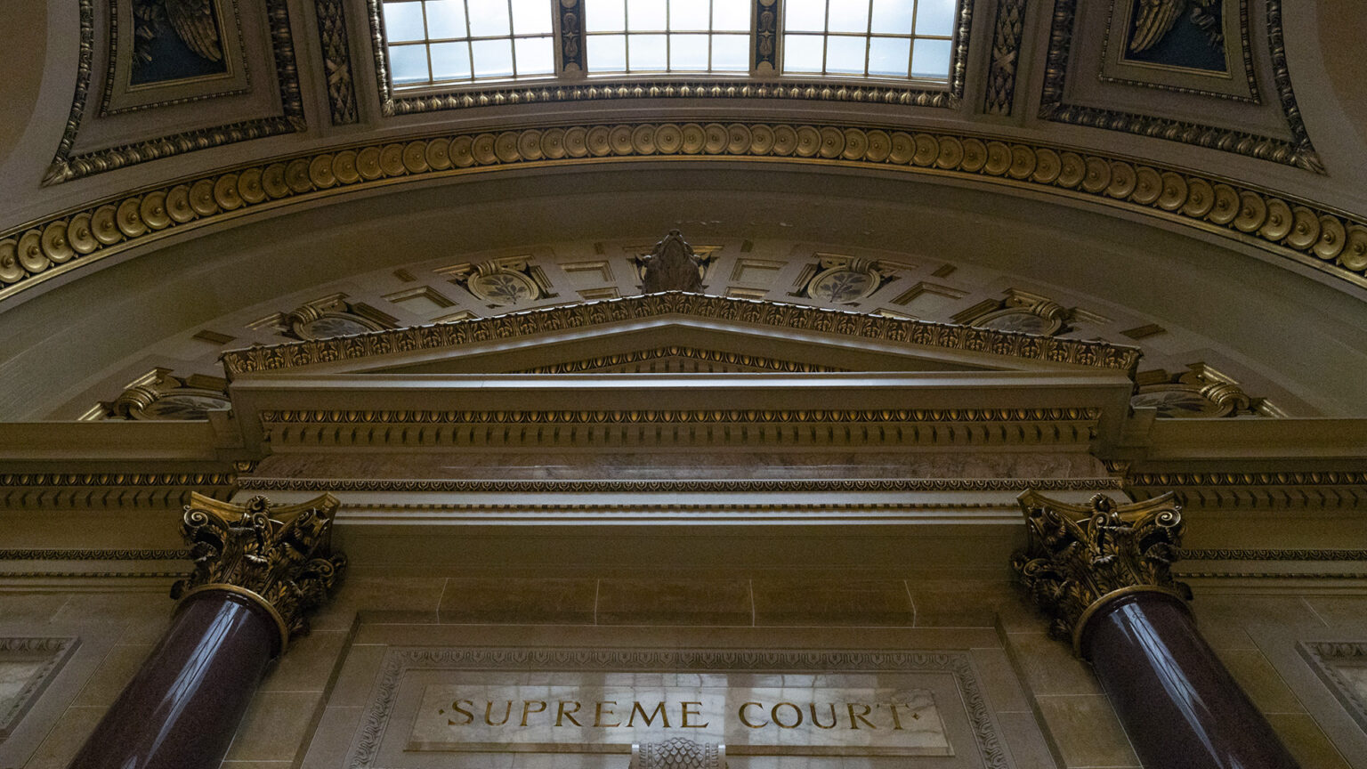 An overhead skylight illuminates marble masonry and two columns with Composite order capitals that flank a carved sign above reading Supreme Court. An overhead skylight illuminates marble masonry and two columns with Composite order capitals that flank a carved sign above reading Supreme Court.
