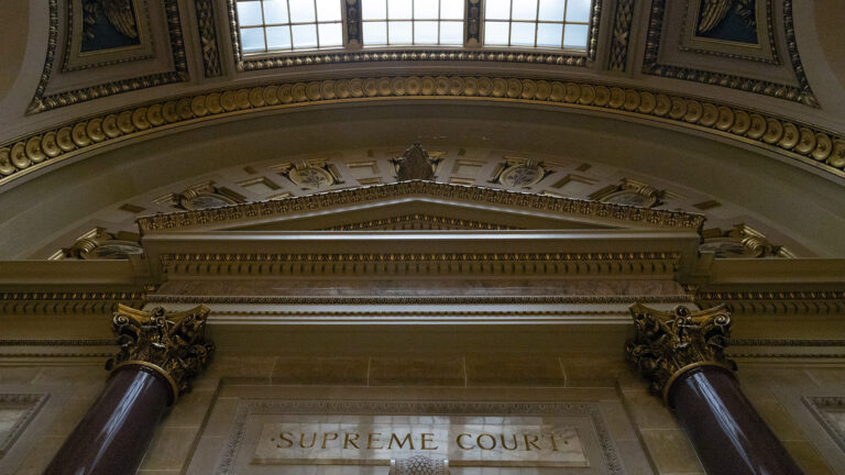 An overhead skylight illuminates marble masonry and two columns with Composite order capitals that flank a carved sign above reading Supreme Court. An overhead skylight illuminates marble masonry and two columns with Composite order capitals that flank a carved sign above reading Supreme Court.