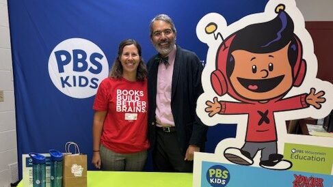 A woman and a man stand at a booth filled with PBS KIDS props and items.