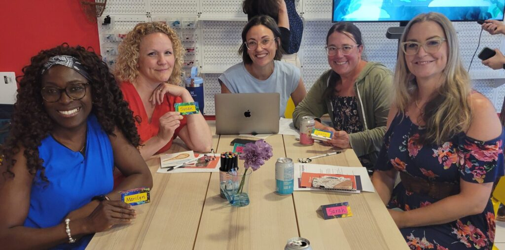 A small group of women sit at a table, smiling at the camera.