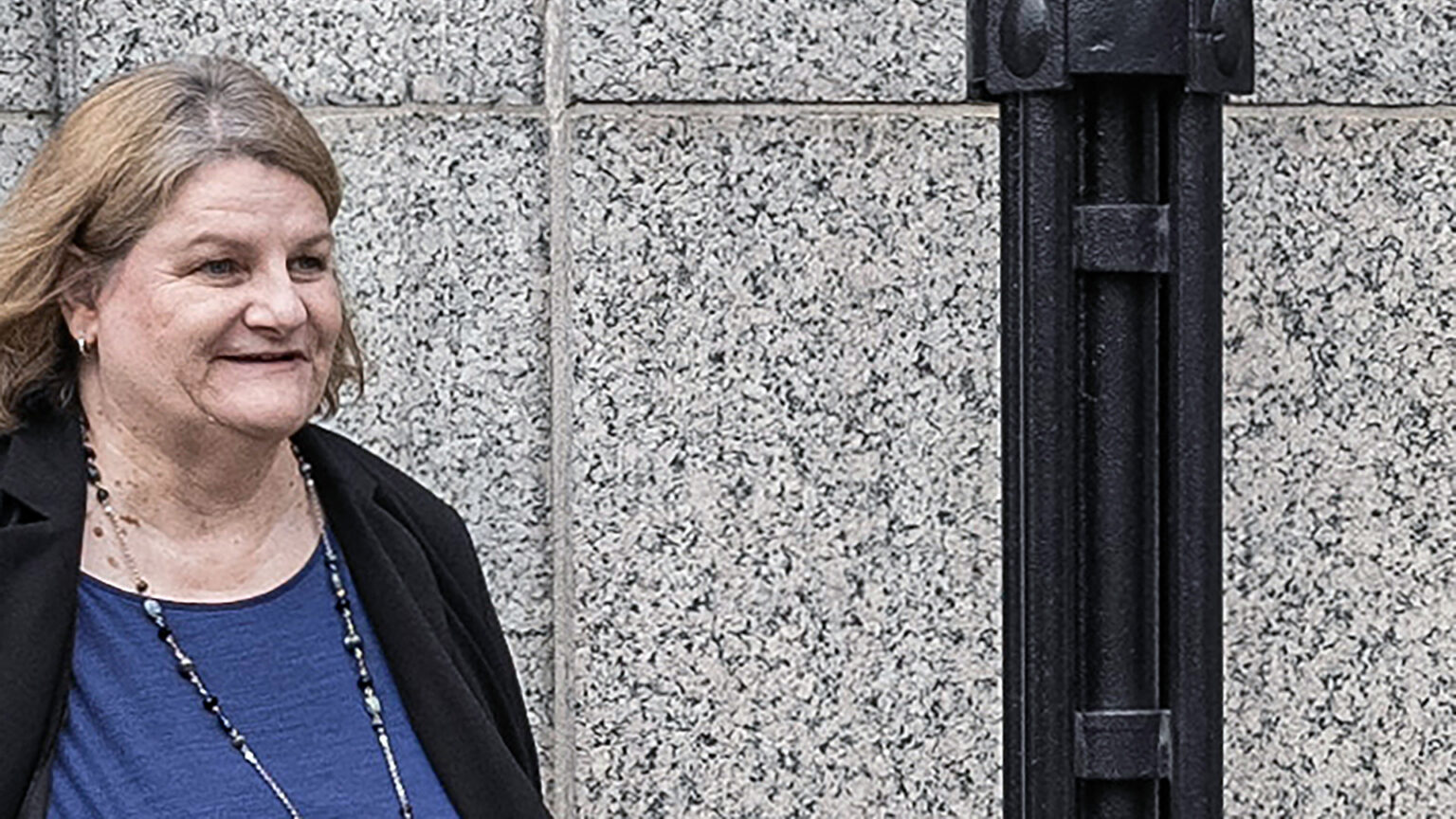 Hannah Dugan walks outside in front of a stone masonry building and next to a metal light fixture.