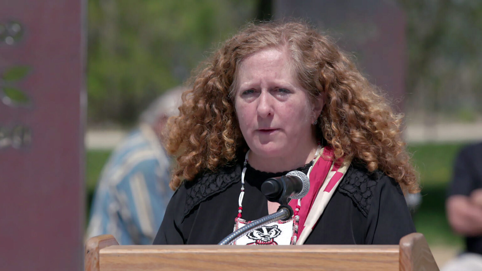 Jennifer Mnookin speaks into a microphone mounted to the top of a wood podium, with out-of-focus metal sculpture elements and seated people in the background. Jennifer Mnookin speaks into a microphone mounted to the top of a wood podium, with out-of-focus metal sculpture elements and seated people in the background.