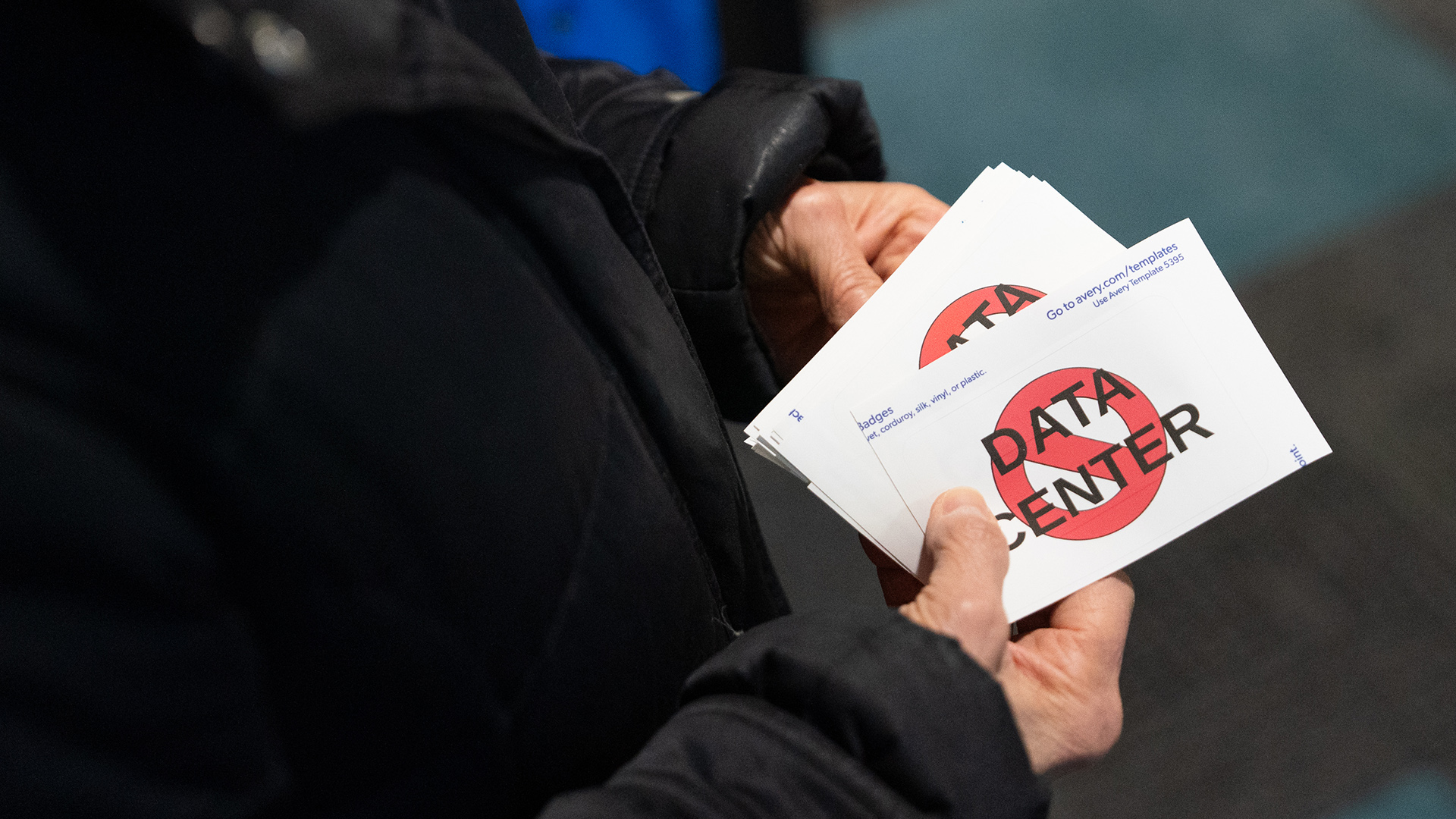 The hands of Sheri Stack hold a stack of stickers with the words "Data Center" superimposed with a no symbol of a circle and a slash.