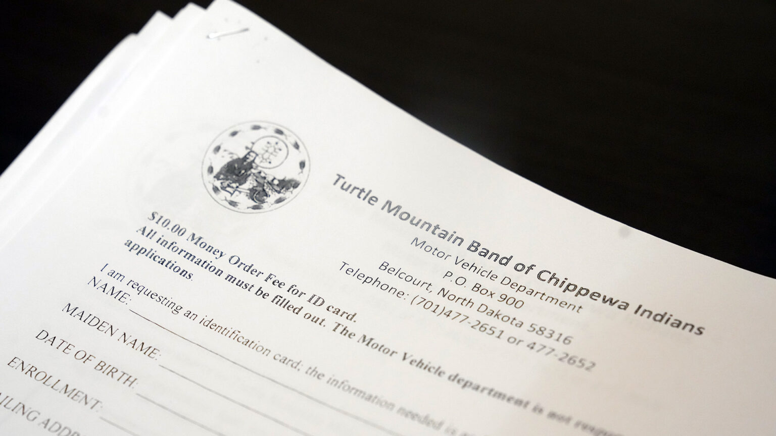 A stapled set of paperwork with a tribal nation logo and the title Turtle Mountain Band of Chippewa Indians along with the text Motor Vehicle Department and an address in North Dakota includes text about a fee and spaces to fill in personal information.
