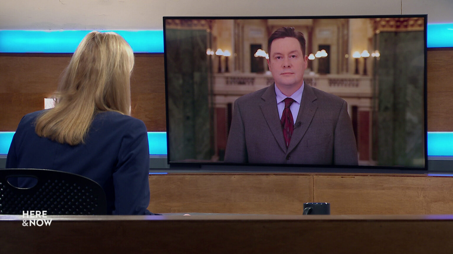 Frederica Freyberg sits at a desk on the Here & Now set and faces a video monitor showing an image of Zac Schultz. Frederica Freyberg sits at a desk on the Here & Now set and faces a video monitor showing an image of Zac Schultz.