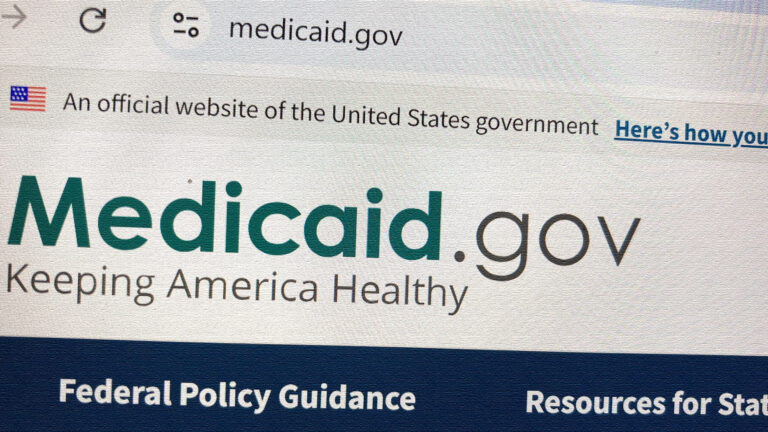A photo shows a website displayed on a Google Chrome browser with a URL bar reading medicaid.gov above lines of text reading An official website of the United States government, Medicaid.gov, Keeping America Healthy, Federal Policy Guidance and other partial phrases.