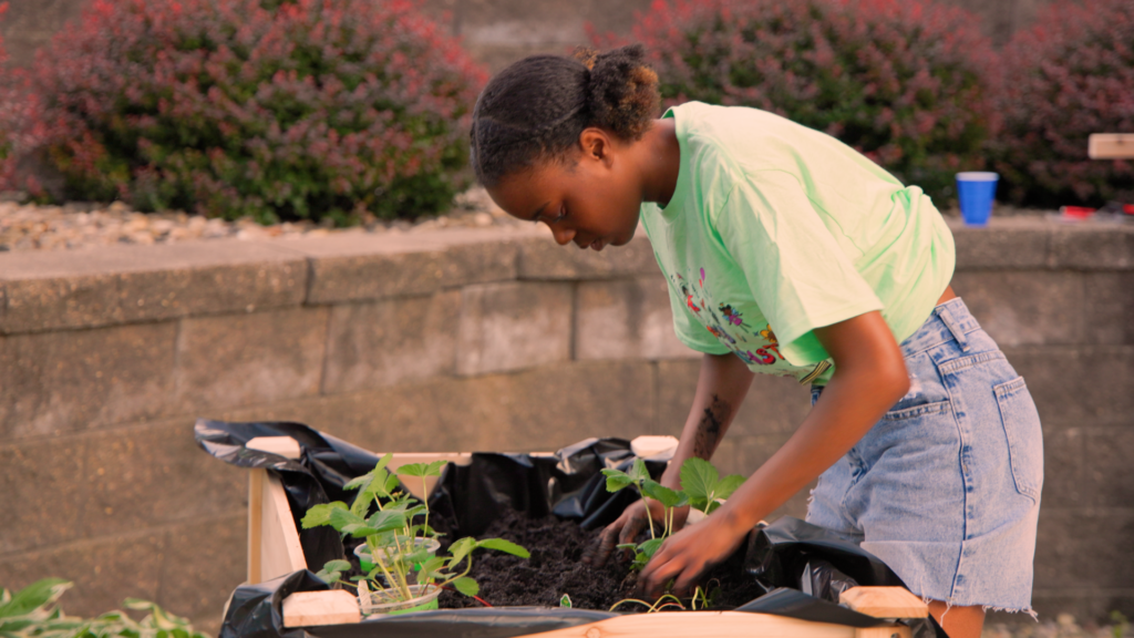 A young person tends to plants in a garden bed.