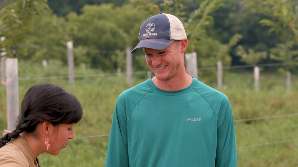A man and woman have a conversation in a farm field.