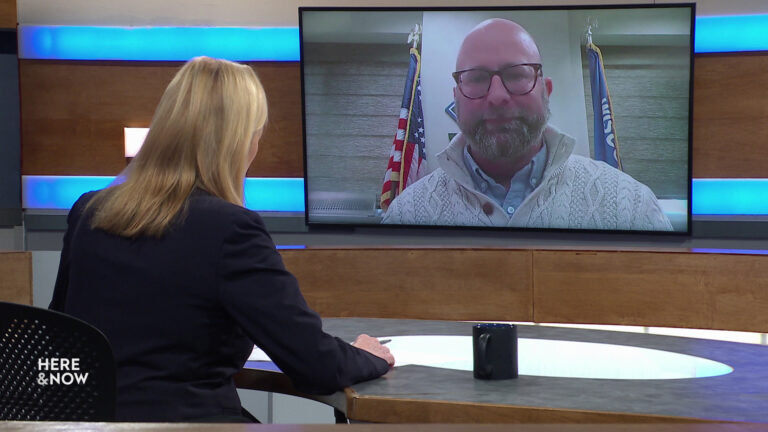 Frederica Freyberg sits at a desk on the Here & Now set and faces a video monitor showing an image of Eric Genrich. Frederica Freyberg sits at a desk on the Here & Now set and faces a video monitor showing an image of Eric Genrich.