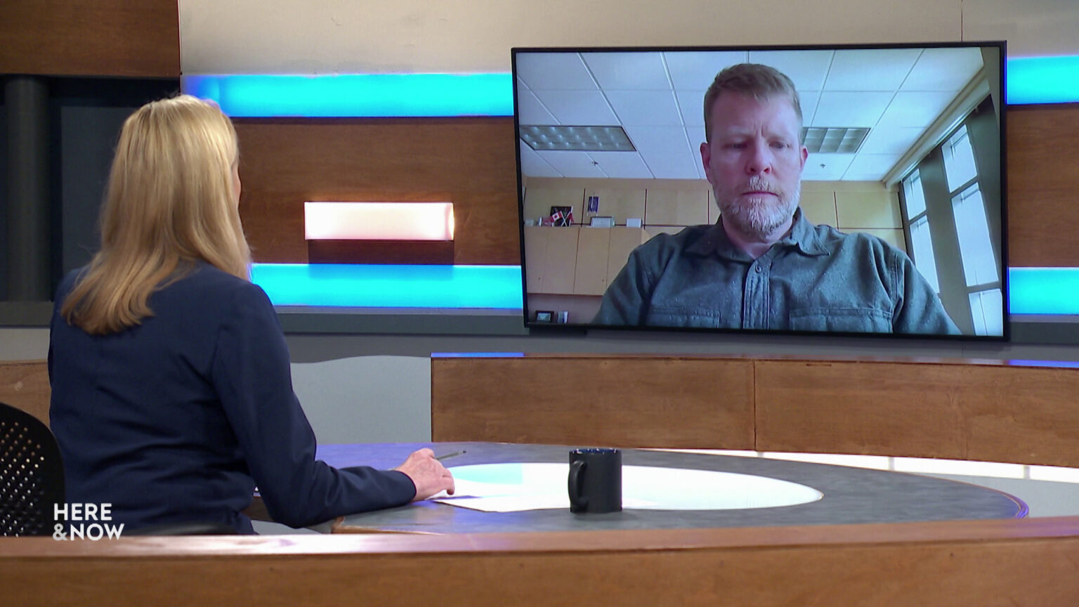 Frederica Freyberg sits at a desk on the Here & Now set and faces a video monitor showing an image of Jim Paine. Frederica Freyberg sits at a desk on the Here & Now set and faces a video monitor showing an image of Jim Paine.