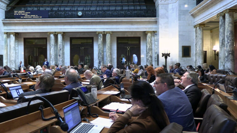 Lawmakers sit in multiple rows of wood desks with microphones, telephones, laptop computers and papers on their surfaces, in a room with marble masonry and pillars supporting second-level seating galleries. Lawmakers sit in multiple rows of wood desks with microphones, telephones, laptop computers and papers on their surfaces, in a room with marble masonry and pillars supporting second-level seating galleries.