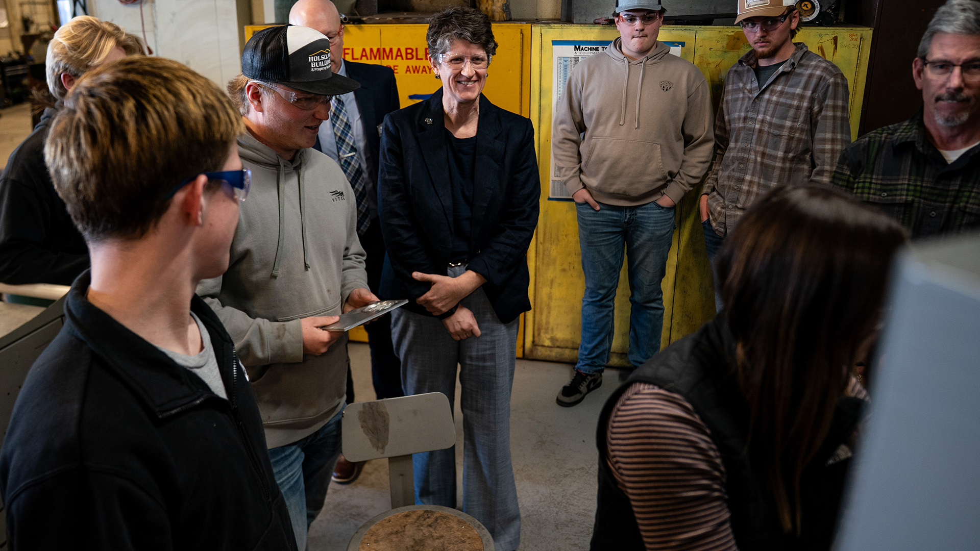 Jill Underly stands while surrounded by other people facing in the same direction in a room with metal cabinets in the background.