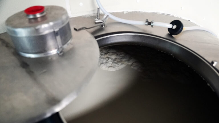 Milk fills a stainless steel tank with an open top and an attached rubber tube.