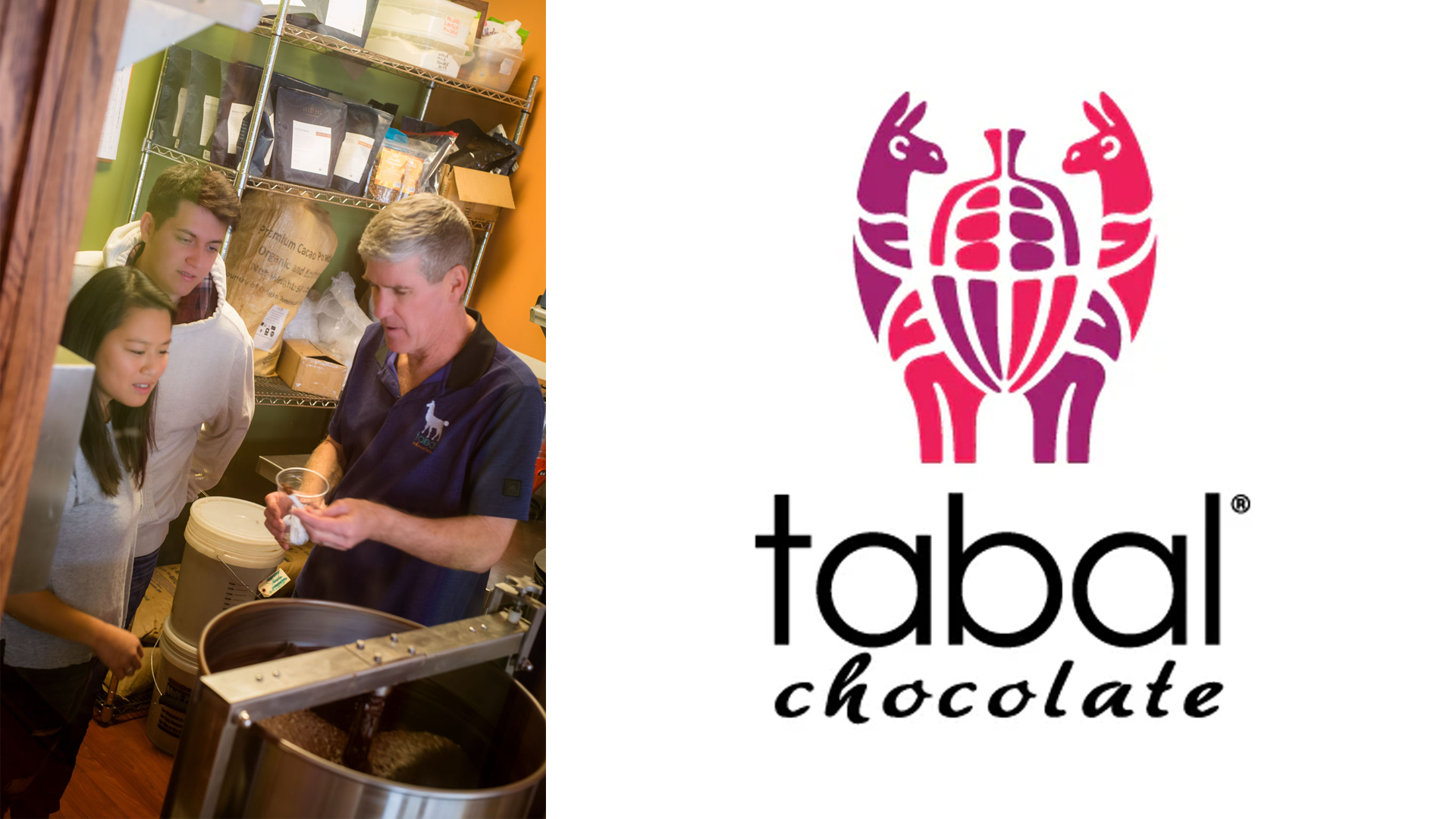 A man explains chocolate-making during a Tabal Chocolate workshop course near a machine, holding a plastic cup, while a woman and man observe. Shelves with ingredients in the background. Nearby, the company's purple and magenta logo with name below.
