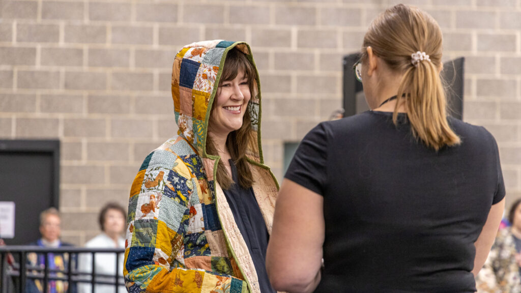 A woman smiles wearing a hooded, quilted jacket.
