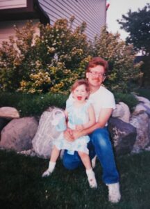 A girl sits on her father's lap outside of a house. They're both smiling.