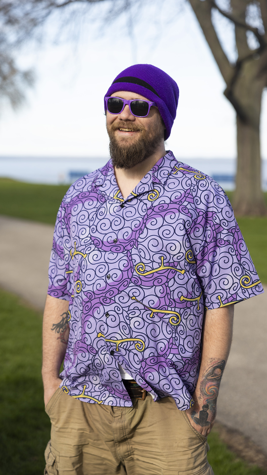 Nikolas DeGroot poses for a photo while standing in front of a sidewalk in a park, with an out-of-focus lawn, tree and lake in the background.