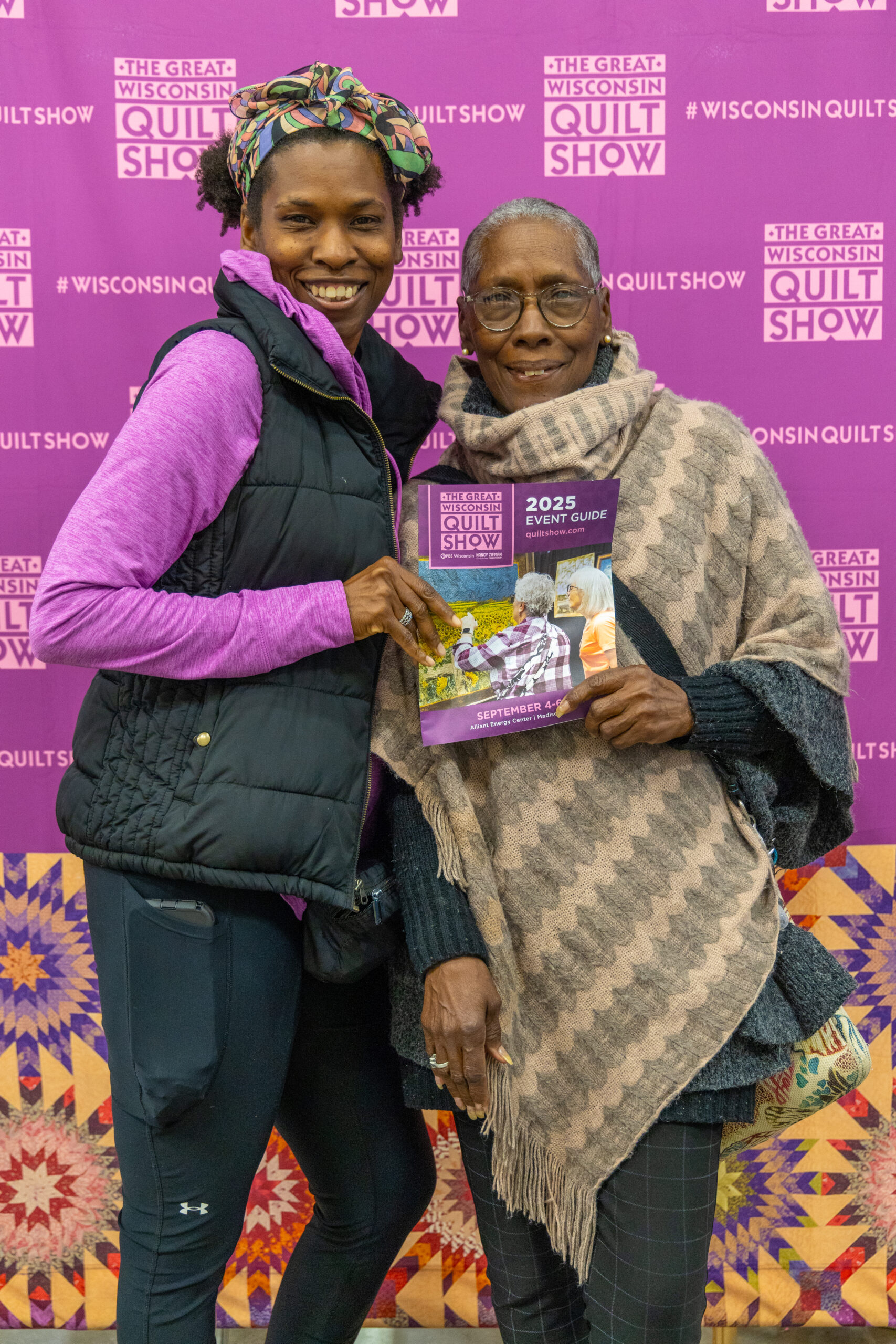 Two attendees pose together holding the 2025 Event Guide in front of the Great Wisconsin Quilt Show step-and-repeat backdrop. (Source: PBS Wisconsin) Two attendees pose together holding the 2025 Event Guide in front of the Great Wisconsin Quilt Show step-and-repeat backdrop. (Source: PBS Wisconsin)