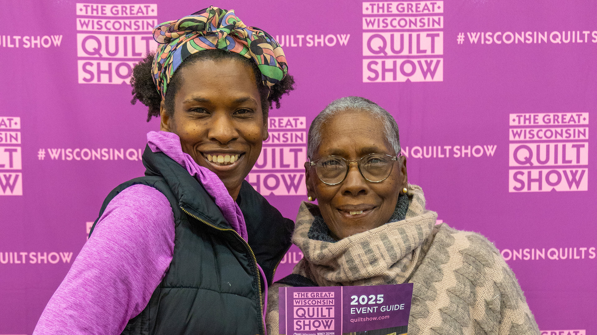 Two attendees pose together holding the 2025 Event Guide in front of the Great Wisconsin Quilt Show step-and-repeat backdrop. (Source: PBS Wisconsin) Two attendees pose together holding the 2025 Event Guide in front of the Great Wisconsin Quilt Show step-and-repeat backdrop. (Source: PBS Wisconsin)