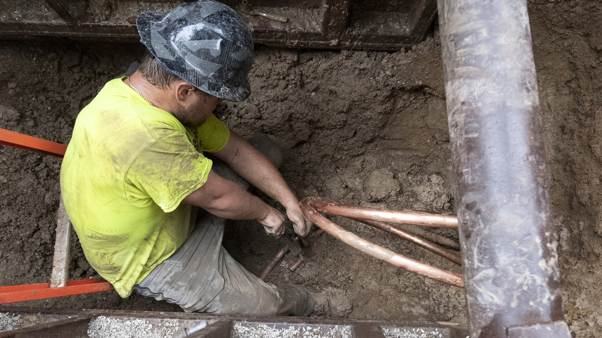 A worker in an excavated pit pulls copper pipes.