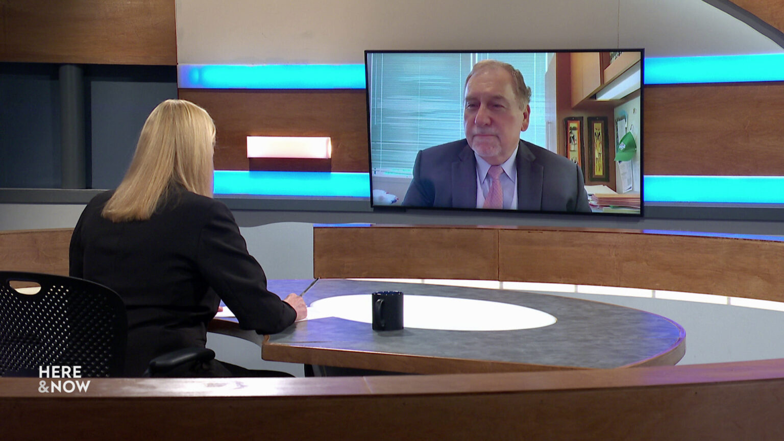 Frederica Freyberg sits at a desk on the Here & Now set and faces a video monitor showing an image of Don Millis. Frederica Freyberg sits at a desk on the Here & Now set and faces a video monitor showing an image of Don Millis.
