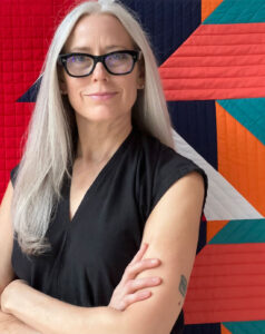 A headshot of Victoria Findlay Wolfe with her quilt in the background.