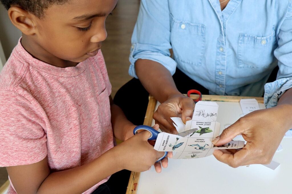 A parent helps a child cut out paper for a game.