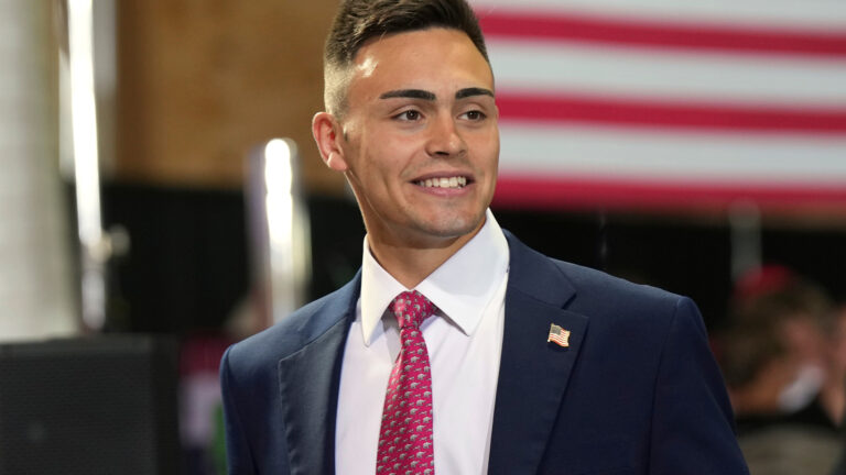 Michael Alfonso smiles while standing in a room with the out-of-focus stripes of a large U.S. flag serving as a backdrop. Michael Alfonso smiles while standing in a room with the out-of-focus stripes of a large U.S. flag serving as a backdrop.