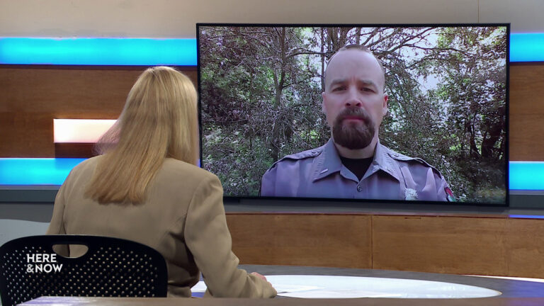 Frederica Freyberg sits at a desk on the Here & Now set and faces a video monitor showing an image of Jake Holsclaw.
