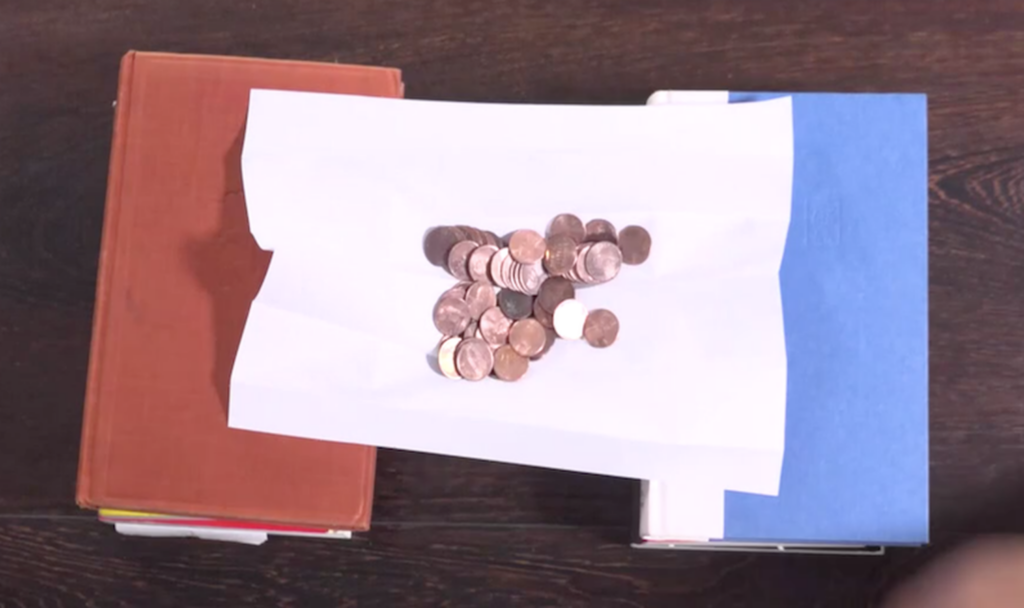 A top-down view of two piles of books with a piece of paper across them. A small piles of pennies is on the paper.