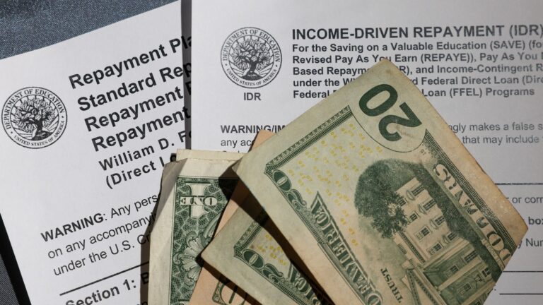 A $20 bill, $10 bill and $1 bill folded in half sit on top of two student loan repayment plan application forms.