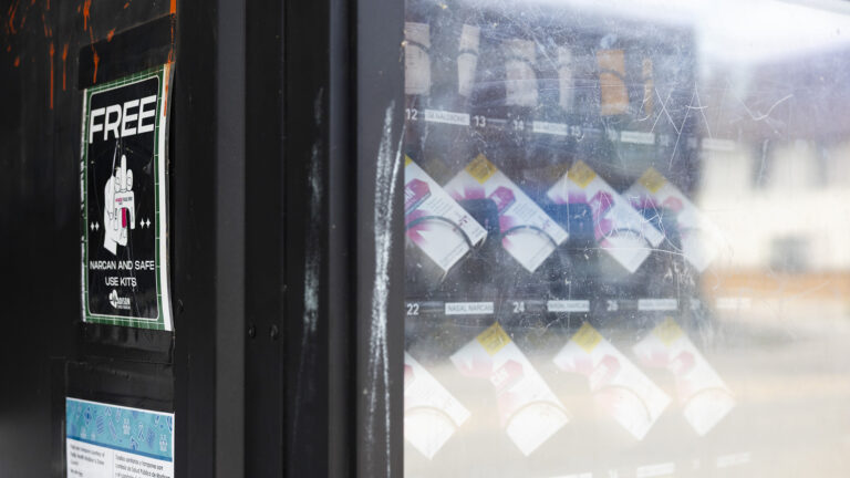 Different items fill a vending machine with a scratched transparent surface and a sign on the side reading Free and Narcan and safe use kits. Different items fill a vending machine with a scratched transparent surface and a sign on the side reading Free and Narcan and safe use kits.