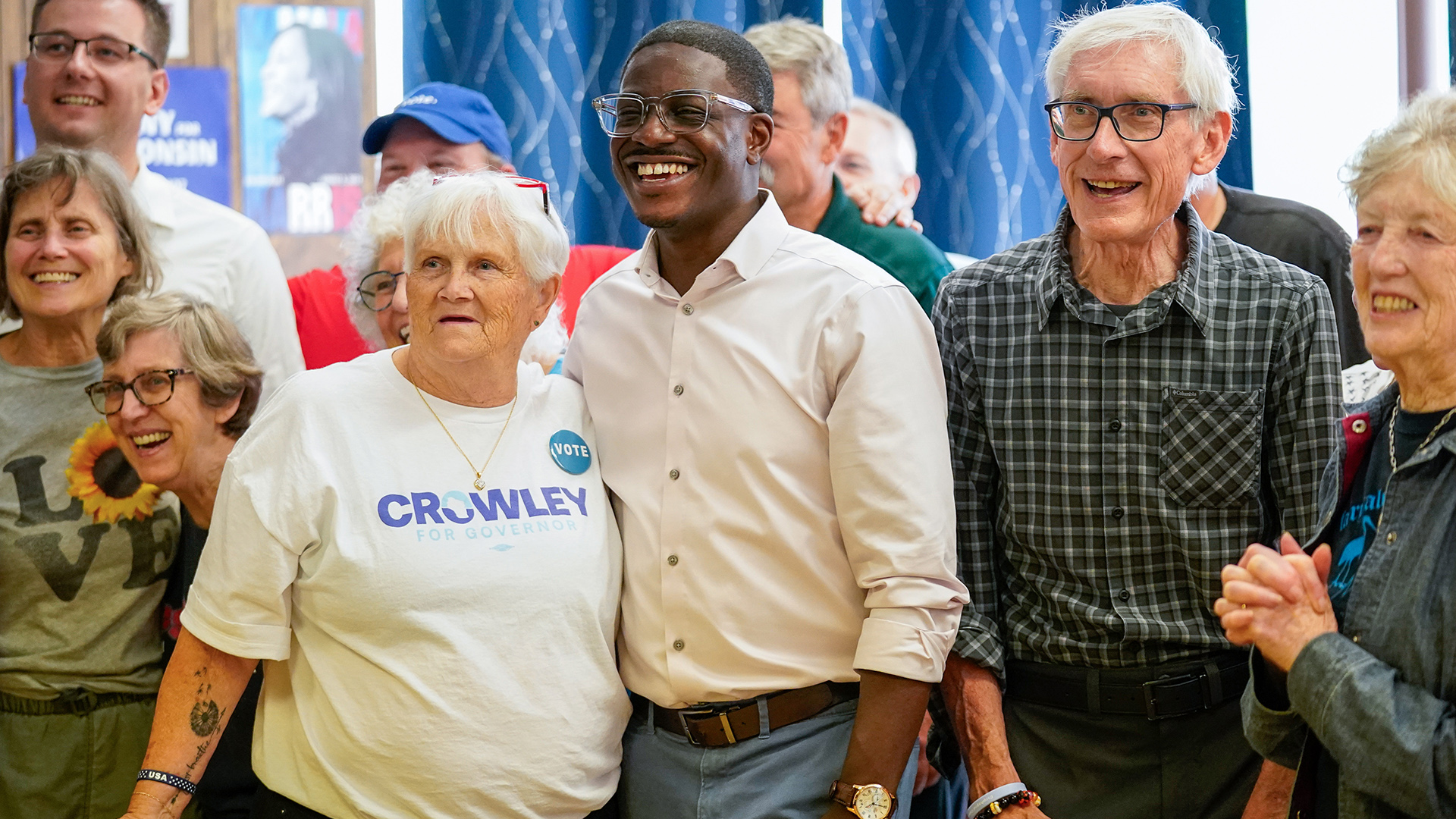 David Crowley and Tony Evers smile while posting for a photo while standing among people on either side of them and in the background.