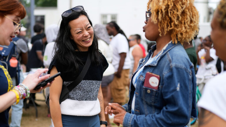Francesca Hong smiles while standing and facing an out-of-focus person in the foreground who is speaking to her, with to more out-of-focus people on either side in the foreground and more out-of-focus people standing in the background. Francesca Hong smiles while standing and facing an out-of-focus person in the foreground who is speaking to her, with to more out-of-focus people on either side in the foreground and more out-of-focus people standing in the background.