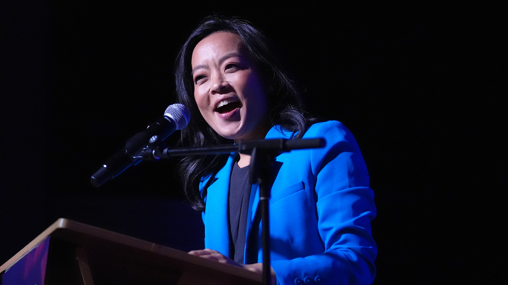Francesca Hong stands and speaks into a microphone mounted to a wood podium.