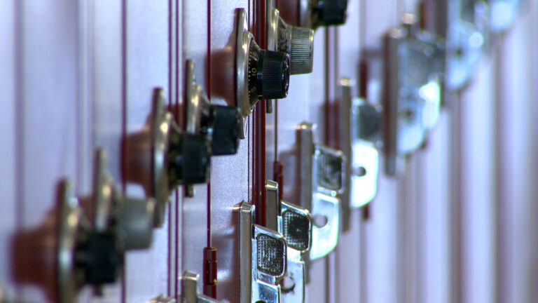 Light reflects off metal latch handles and rotary combination locks integrated into a row of metal school lockers.
