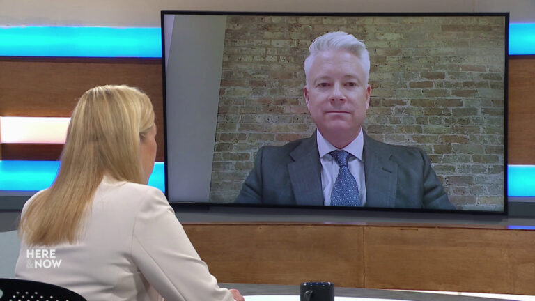Frederica Freyberg sits at a desk on the Here & Now set and faces a video monitor showing an image of John Miller. Frederica Freyberg sits at a desk on the Here & Now set and faces a video monitor showing an image of John Miller.