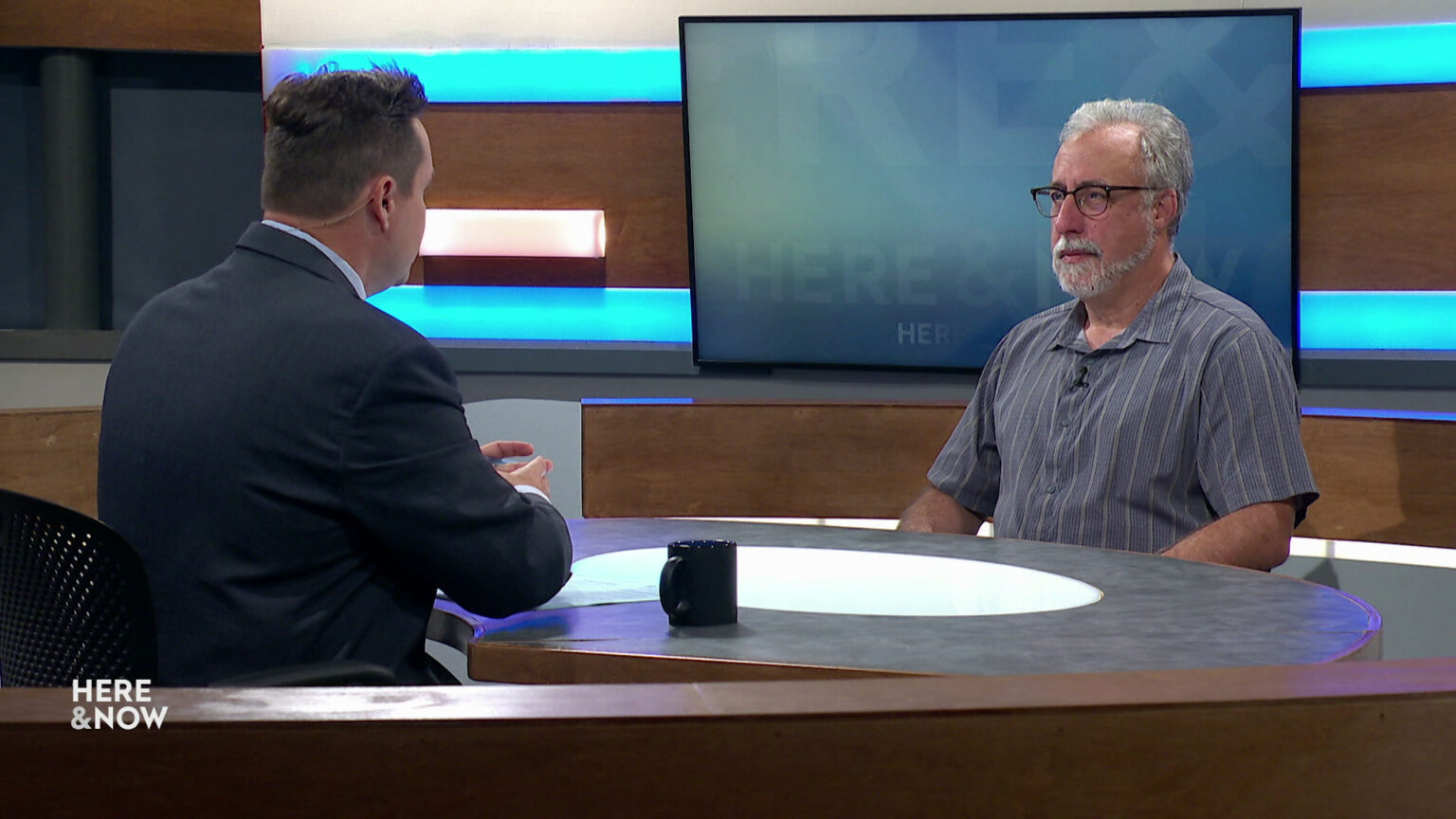 Zac Schultz and Howard Schweber sit facing each other on the Here & Now set.