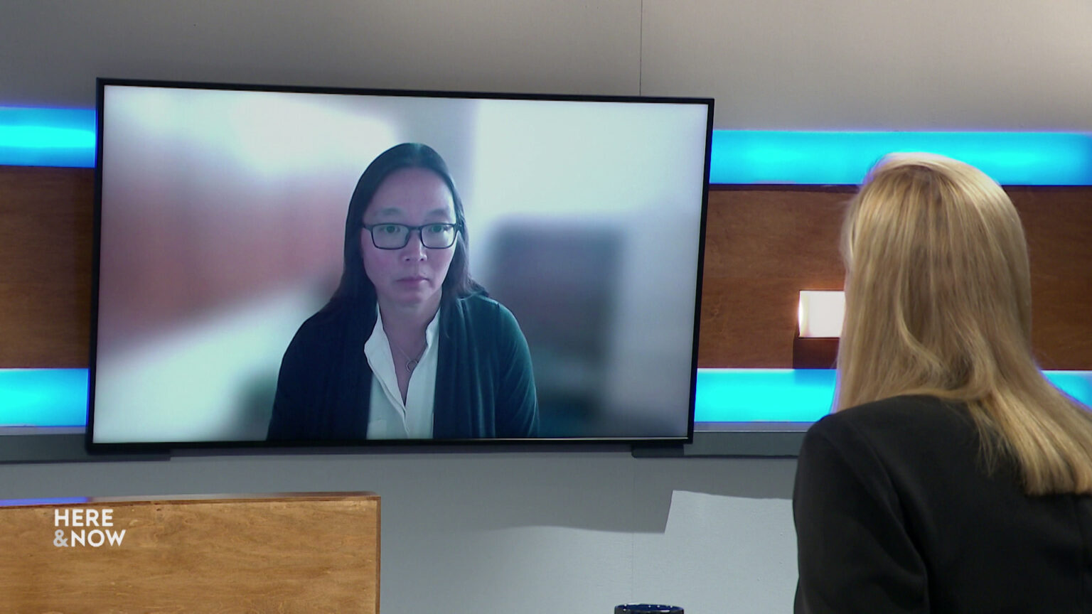 Frederica Freyberg sits at a desk on the Here & Now set and faces a video monitor showing an image of Karen Hyun. Frederica Freyberg sits at a desk on the Here & Now set and faces a video monitor showing an image of Karen Hyun.
