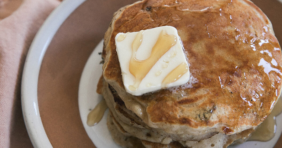 Stack of pancakes covered in syrup and a slab of butter on a plate.