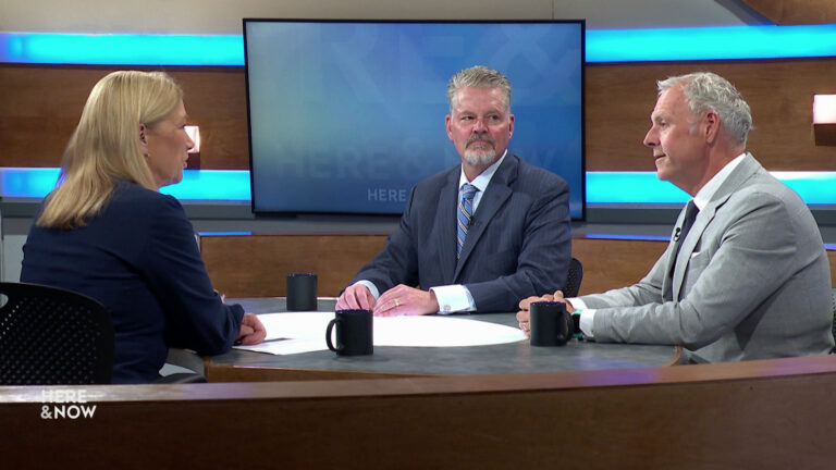 Bill McCoshen and Scot Ross sit next to each other and across from Frederica Freyberg at a desk on the Here & Now set.