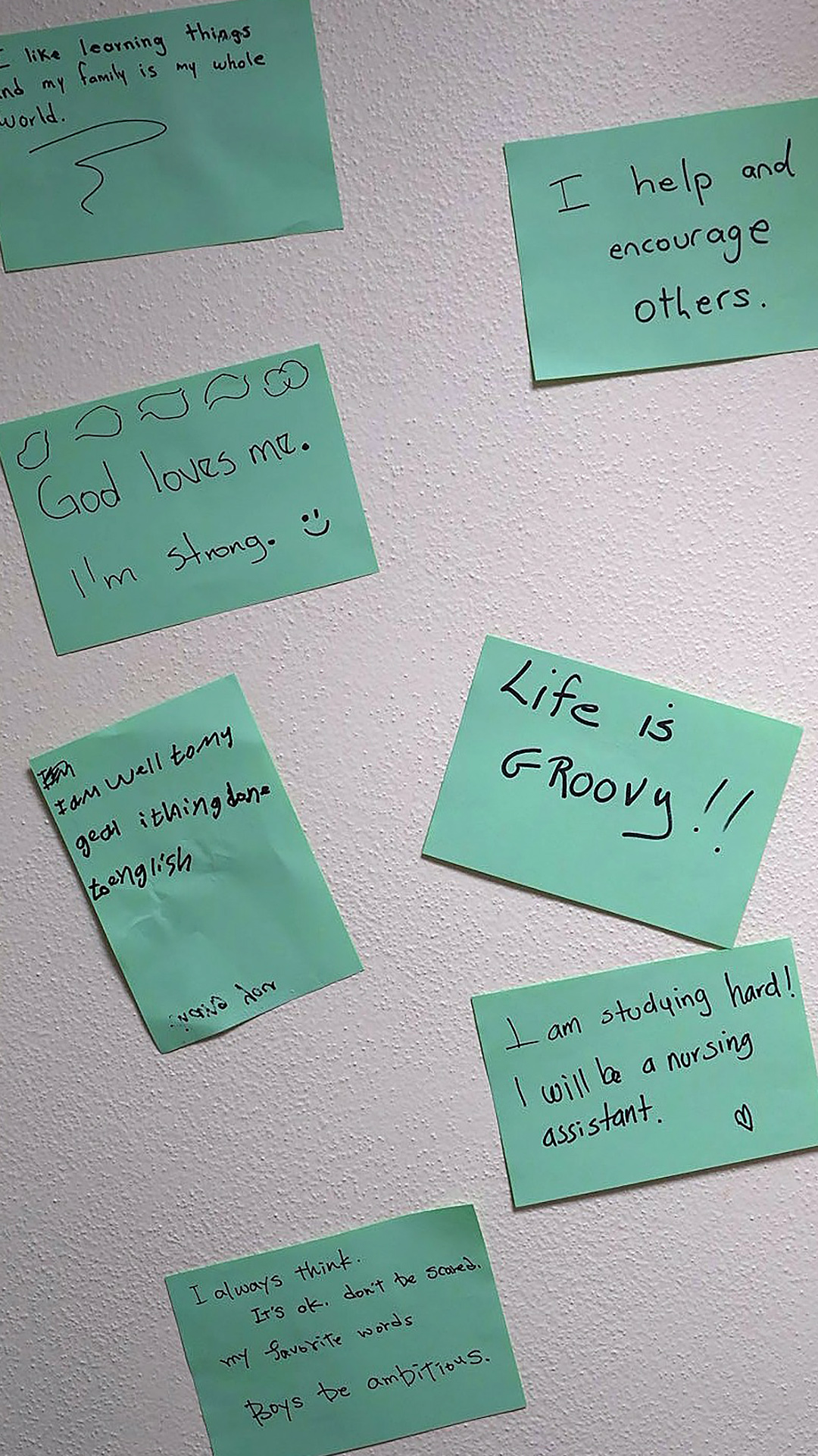 Multiple handwritten notes are affixed to the surface of a wall.